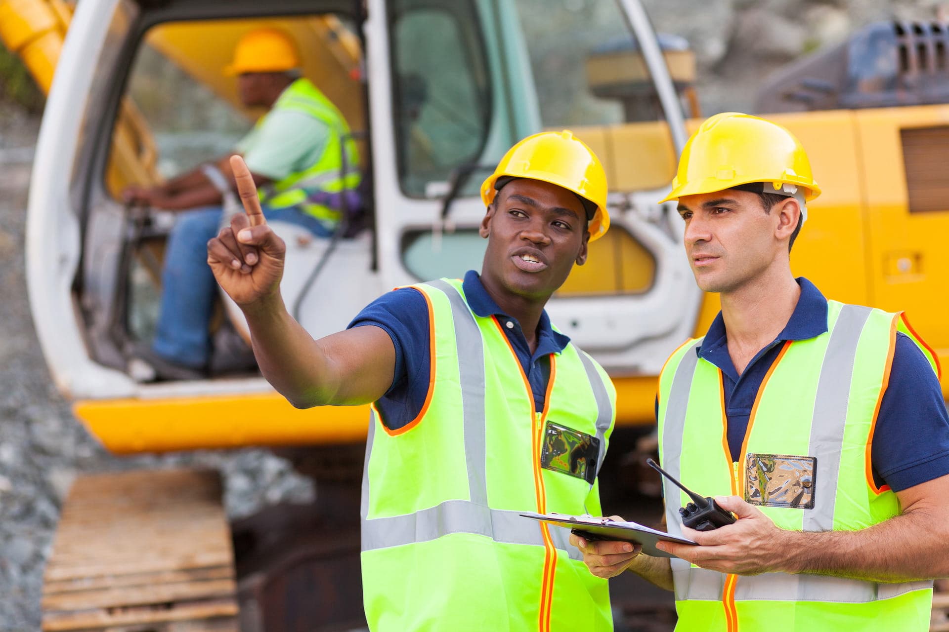 Two site workers in hi-vis in front of an excavator